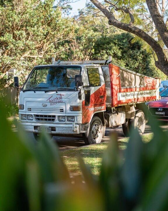 A Tomkat Roofing truck with a branded logo and tagline, parked in a residential area.