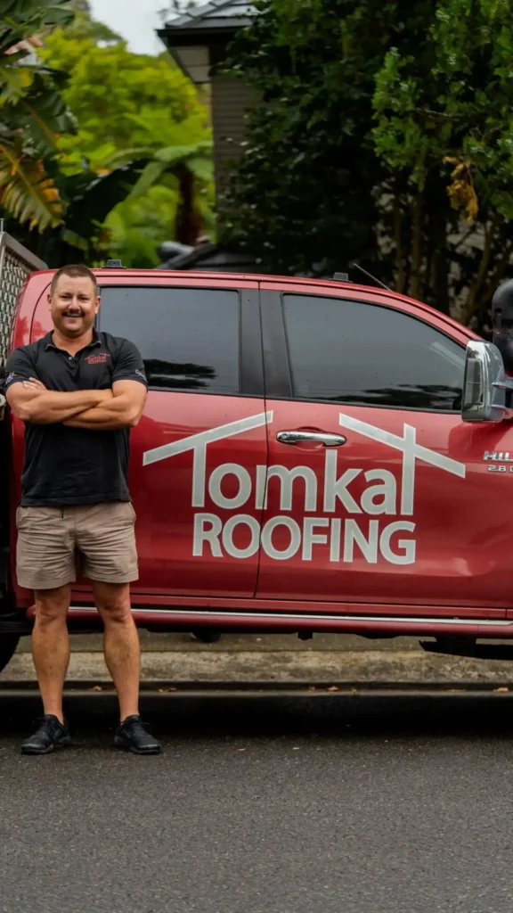 Tomkat Roofing contractor standing by branded red vehicle in Sydney neighborhood.