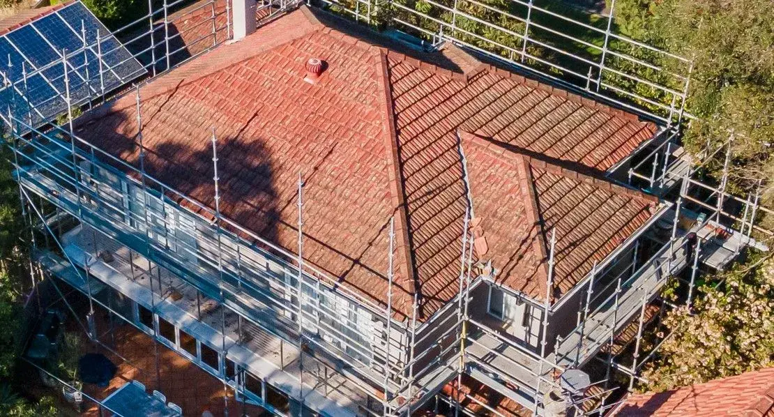 Residential roof restoration with scaffolding installed around tiled roof for repair and maintenance work